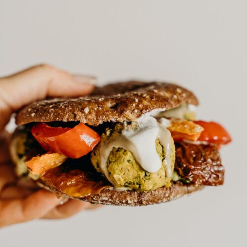 Hand holding a delicious falafel sandwich with vibrant vegetables and creamy sauce.