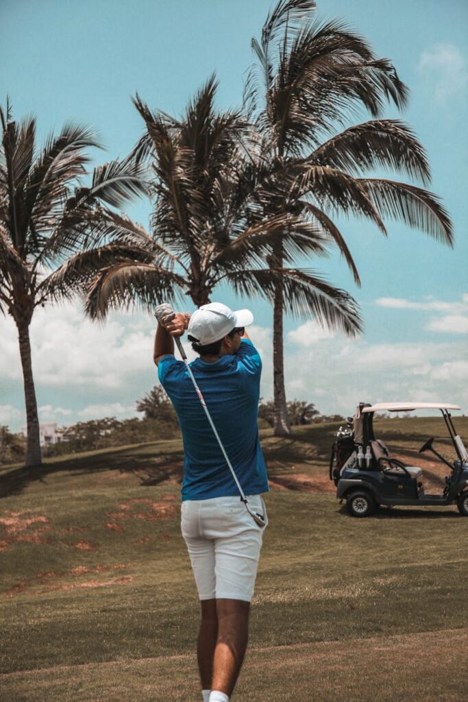 Golfer in blue polo swings on a sunlit course with palm trees, Puerto Vallarta.