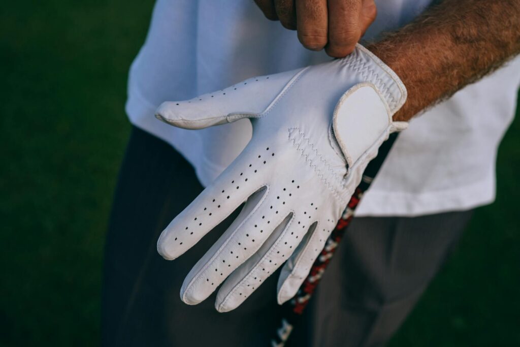 Close-up of a golfer adjusting their white glove with a club, outdoors.